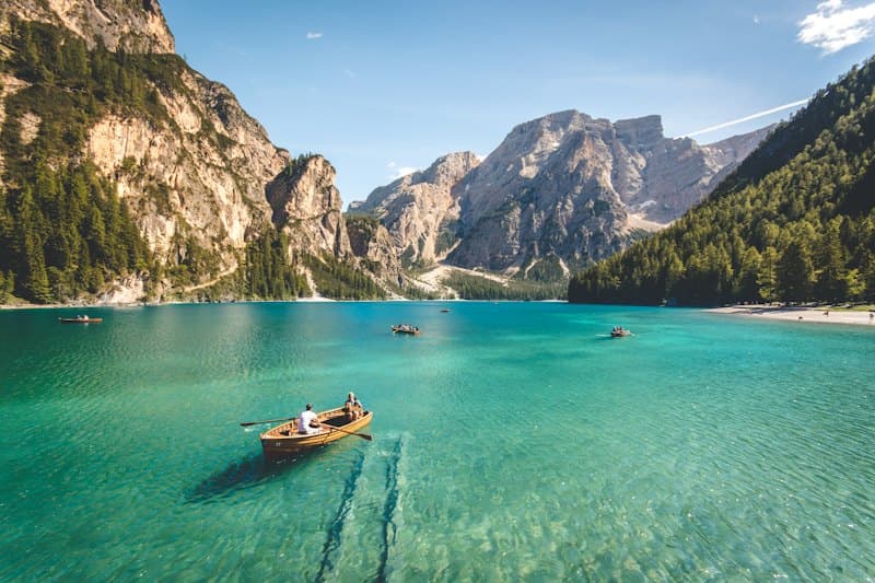 A wooden rowing boat on a clear turquoise lake ringed by forest and rocky peaks
