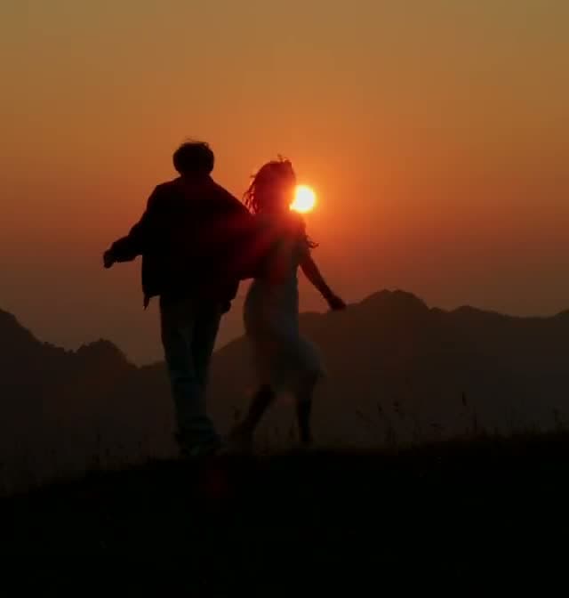 A couple dancing on a ridge at sunset, in silhouette