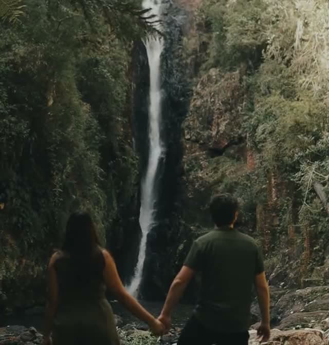 A couple holding hands in front of a waterfall